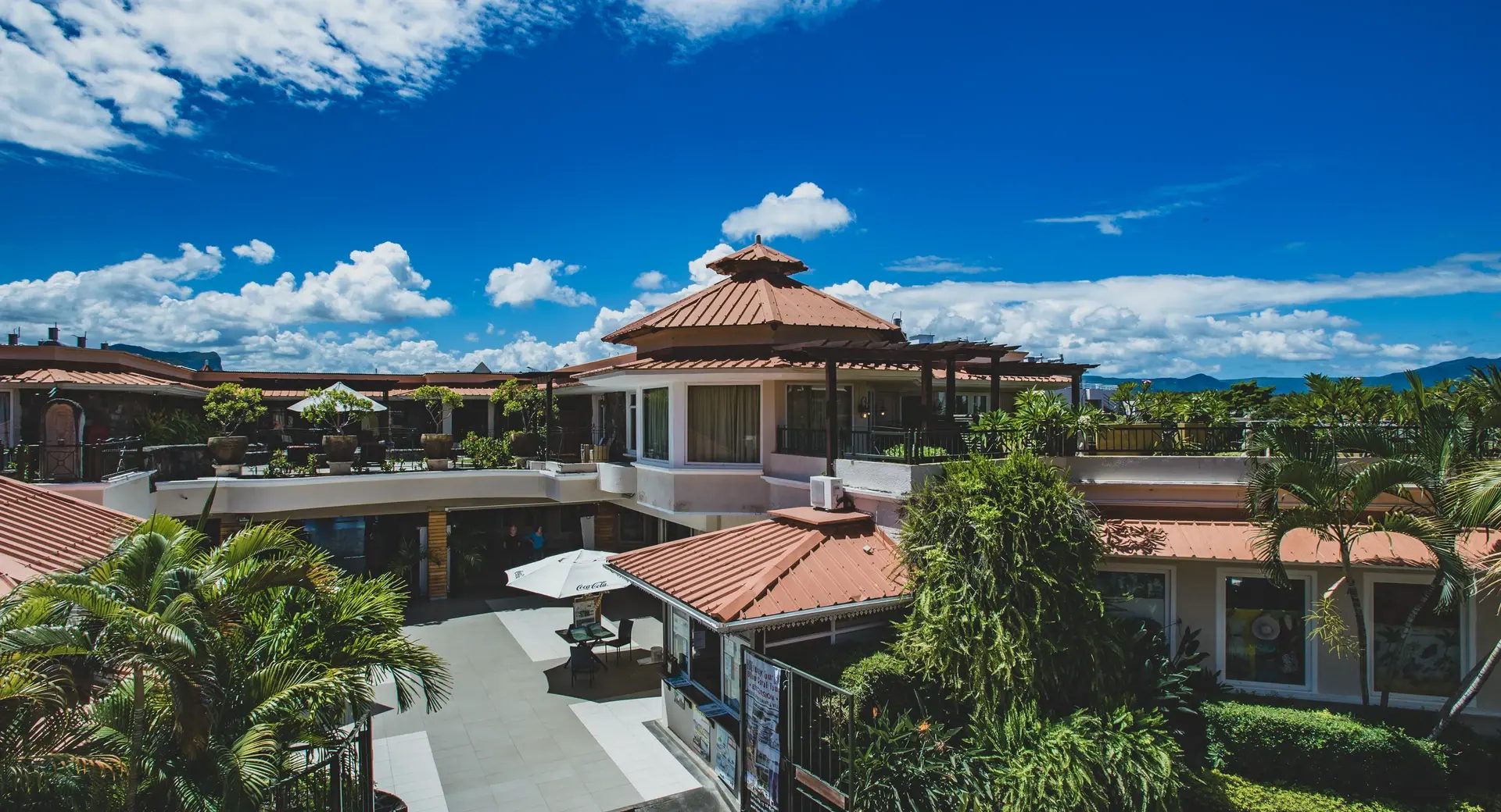 Resort courtyard with red roofs, a rooftop terrace and palm gardens under a blue Mauritian sky